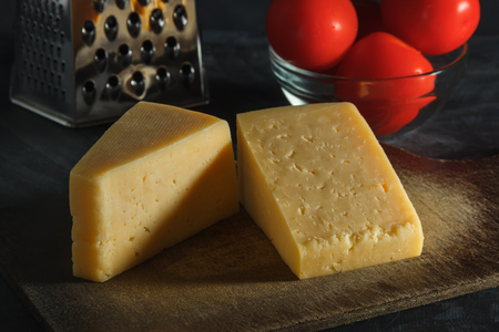 Two pieces of cheese, tomatoes and grater on a board on a dark backgroundの写真素材