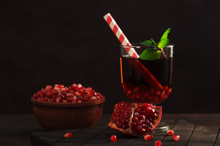 Pomegranate juice in a glass with straw and fruit in the bowlの写真素材