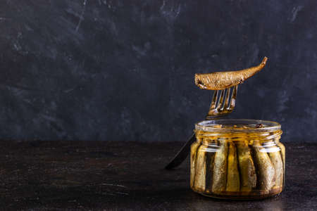 Glass open jar of sprots and fish on a forkの写真素材