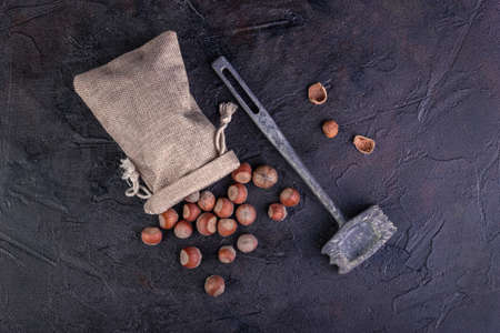 Hazelnuts in a bag and hammer against a dark background