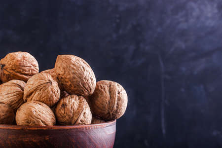 Full clay bowl with walnut on a dark background. Copy space.
