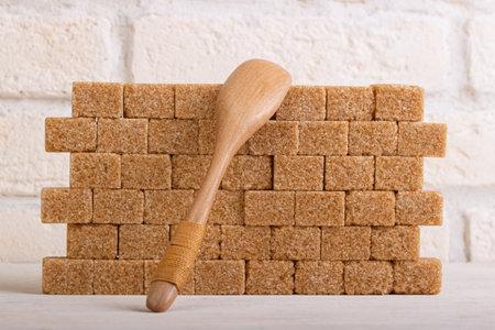 A wall of brown cane sugar cubes with a wooden spoonの写真素材