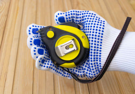 Yellow measuring tape in the hand of a worker - with protective gloves.