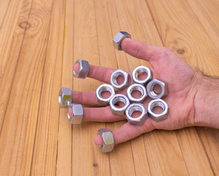 Metal shine nuts in the hand of the workerd - Wooden background.