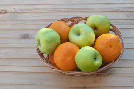 Oranges and apples in a basket on wooden background.の写真素材