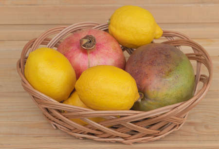 Mango lemon and pomegranate in a basket - fruit health benefits concept - wooden background.の写真素材