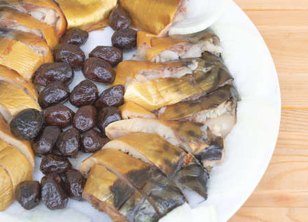 Marinated fish and olives in a white plate close up - Wooden background.