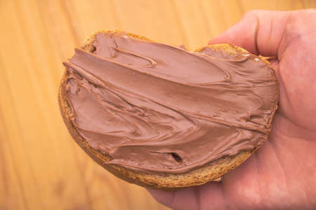 Delicious cocoa cream greased on a slice of bread - in the hand of a man.