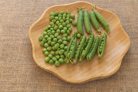 Closeup shot of fresh green peas on a wooden plate.