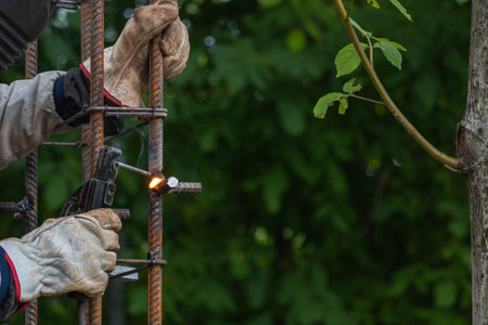 A worker welds a reinforcement - future column - construction concept. Green trees background.の写真素材