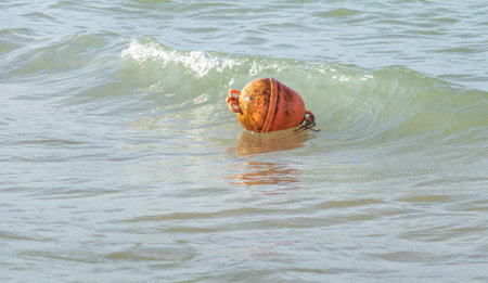 Orange buoy floating in the sea with water splashes on it.