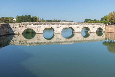 The ancient bridge over the river in Rimini, Italy which is Ponte di Tiberio with a clear blue sky and reflection in the waterの写真素材