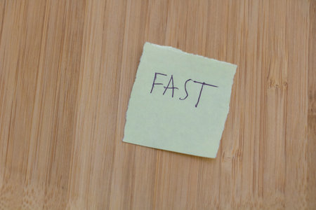 A photo of the text FAST written on a sticky note, isolated on a wooden background in a close up...