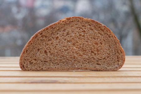 A slice of whole-wheat bread sitting on top of a wooden table, in a flat front view, with a window...