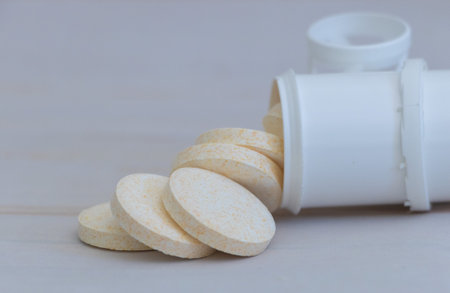 Close-up of a round, beige and white medicine tablet spilling out from an open pill bottle on a light background.の写真素材