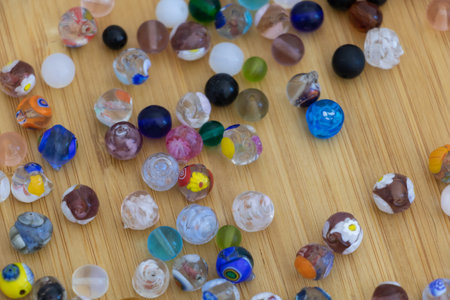 A close-up of various glass beads scattered on the table, including round and oval shapes with...