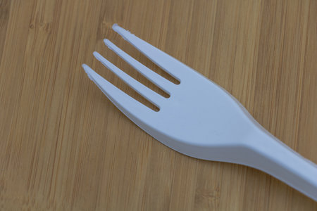 White plastic fork on a wooden table, close-up of a product photo.