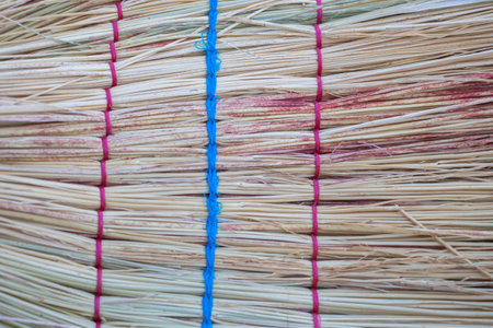 A close-up of the back of a broom made from paddy sticks with pink and blue twine tied around it, against a textured backgroundの写真素材