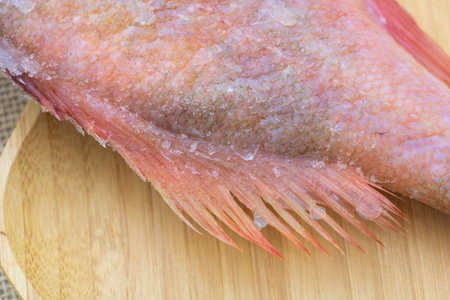 Close-up of a pink red fish on a wooden plate. The entire body is covered in ice crystals, in a...