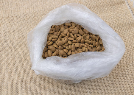 A white plastic bag filled with dog food on the table, top view. The background is burlap fabric.