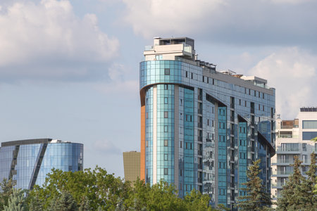 A modern high-rise building in the center along with other buildings and trees nearby.の写真素材