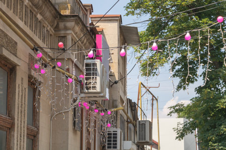 An urban street in the city center decorated with pink and white decorations for a birthday celebration. Pink balloons on wires are hanging from power lines above the housesの写真素材
