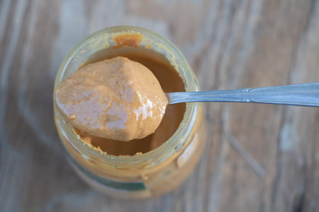 A spoonful of peanut butter is being taken from an open jar on the table, in a top-down view.の写真素材