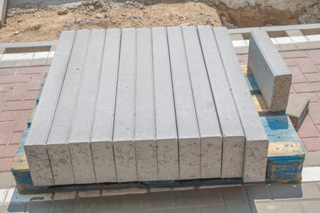 A stack of gray pavers on pallets, concrete pavers with blue edges, sitting in the street next to a construction site.の写真素材