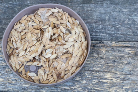 Bowl filled with melon seeds placed on rustic wooden surface, ready for drying or planting.の写真素材