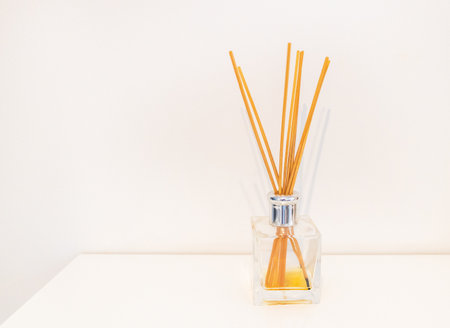 Minimalist home fragrance reed diffuser with orange sticks on white background.