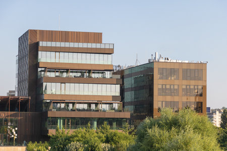 Sleek Modern Office Complex with Bronze-Tinted Glass Facade Amidst Lush Greenery at Golden Hour.の写真素材