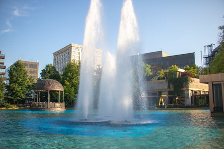 Ornate Iron Gazebo Beside Towering Blue Fountain Jets in an Urban Plaza at Sunrise.の写真素材