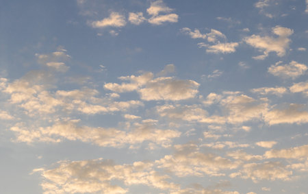 Golden-hued clouds scattered across a soft blue sky during sunrise or sunset.