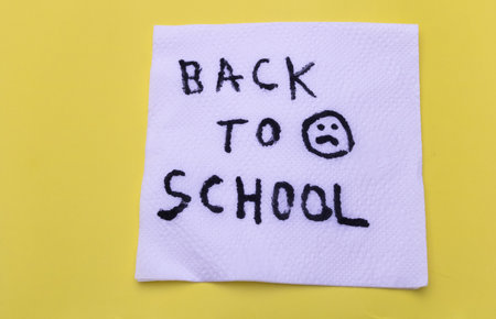 White napkin with handwritten Back to School message and sad face on yellow background.