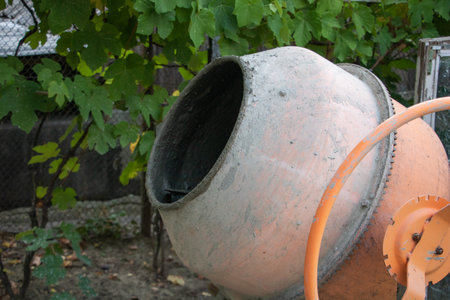 Old Concrete Mixer in Outdoor Setting with Green Foliage Background.の写真素材