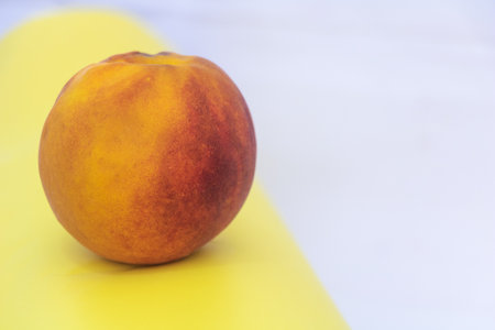 Single fresh ripe peach fruit on colorful yellow and white background, organic summer food closeup...