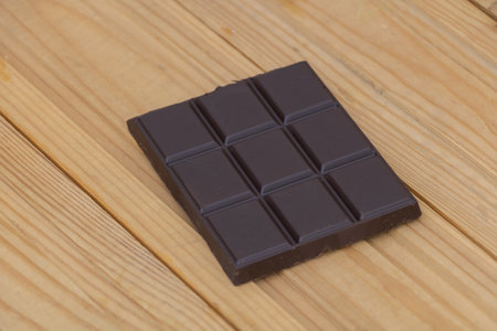 Dark chocolate bar with square pieces placed on wooden background, sweet dessert concept with rich cocoa flavor.の写真素材
