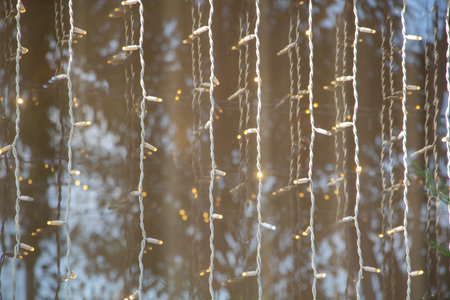 Decorative string lights glowing with warm yellow bulbs hanging vertically on transparent surface,...