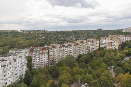 Panoramic city view showing residential apartment buildings and green forest hills under cloudy...