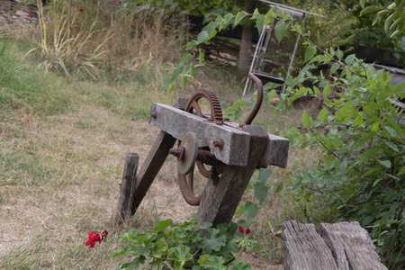 Old wooden and metal mechanical gear structure from traditional farm equipment surrounded by grass and plants in countryside.の写真素材