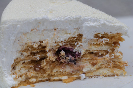 Slice of layered cream cake with nuts and berry filling, showcasing fluffy frosting and sweet...