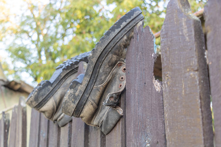 Old worn work boots hanging on a wooden fence outdoors, symbolizing rural lifestyle and hard labor backgroundの写真素材