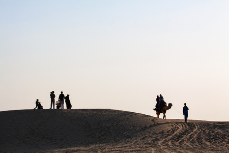 Silhouetted Family Group with Children watching sunset  Couple on Camel being led away by handler  sand dunes  with clear blue evening skyのeditorial素材