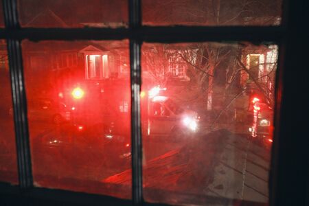 Nighttime red emergency lights flashing in residential neighborhood as seen from upstairs window.