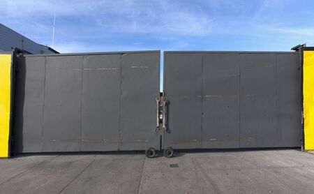 Closed industrial yard gate with driveway and blue sky.の写真素材