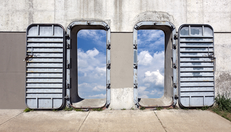 Steel and concrete industrial wall and doors opening onto sky.の写真素材