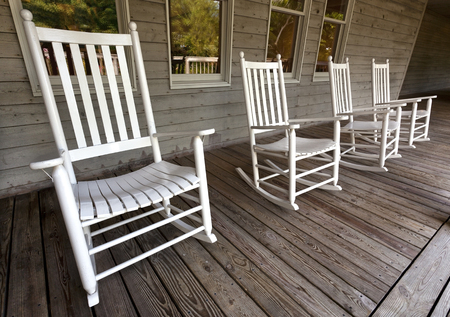 Four white rocking chairs on wooden porch.の写真素材