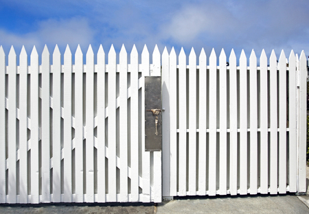 Elegant and simple white wood picket fence and gate under blue sky.の写真素材