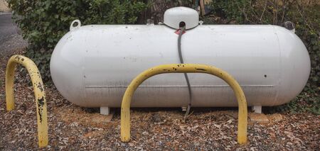 Large propane liquid gas tank protected with yellow metal bollards.