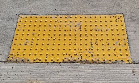 Yellow bumpy tactile sidewalk ramp pad alerting pedestrians they are approaching a sidewalk.の写真素材